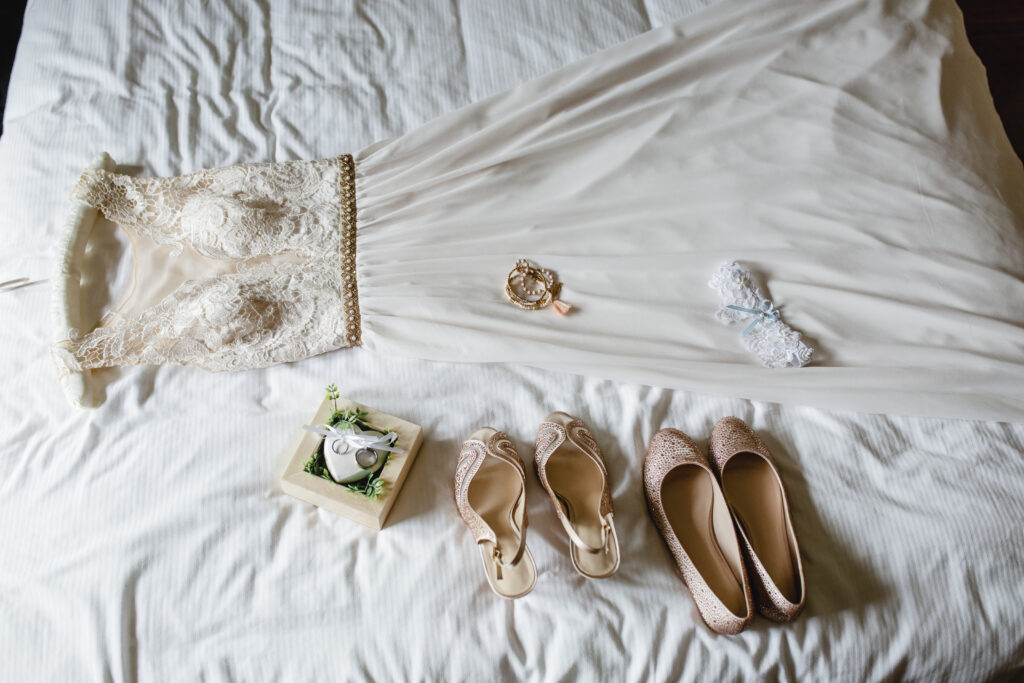 Letto con sopra un abito da sposa bianco, scarpette e fedi nuziali, pronto per il grande giorno